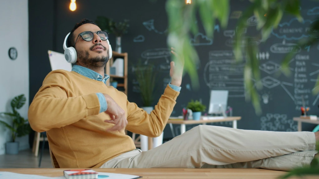 Man in headphones playing air guitar in office.